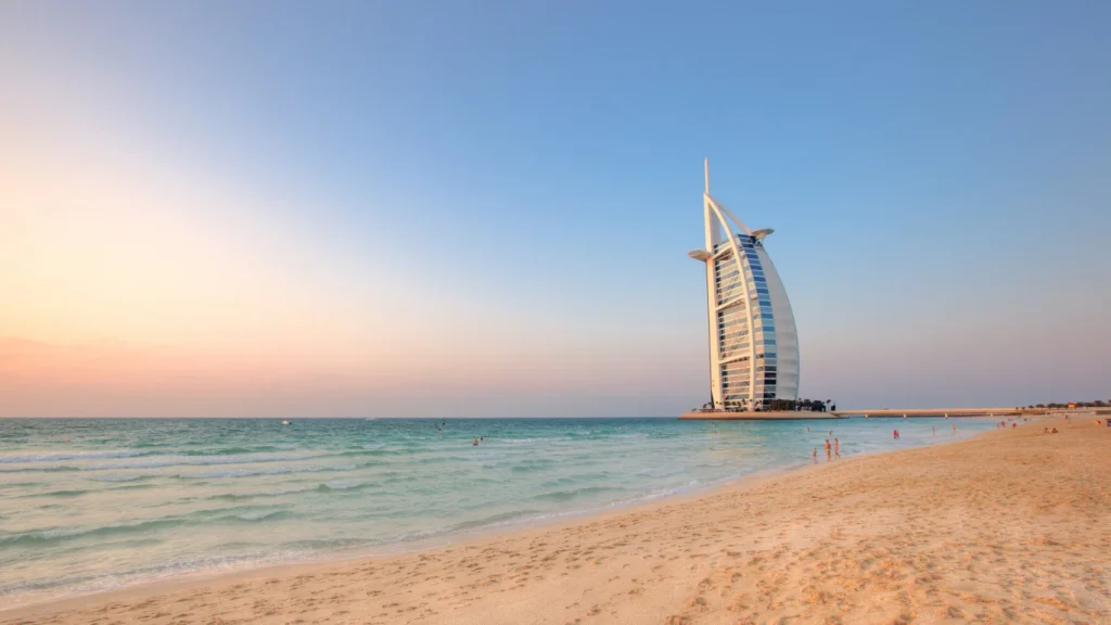 Stunning postcard-like view of Al Sufouh Beach with the iconic Burj Al Arab, pristine sand, and gentle waves rolling onto the shore at sunset.