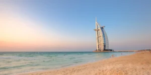 Stunning postcard-like view of Al Sufouh Beach with the iconic Burj Al Arab, pristine sand, and gentle waves rolling onto the shore at sunset.