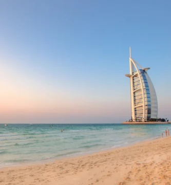 Stunning postcard-like view of Al Sufouh Beach with the iconic Burj Al Arab, pristine sand, and gentle waves rolling onto the shore at sunset.