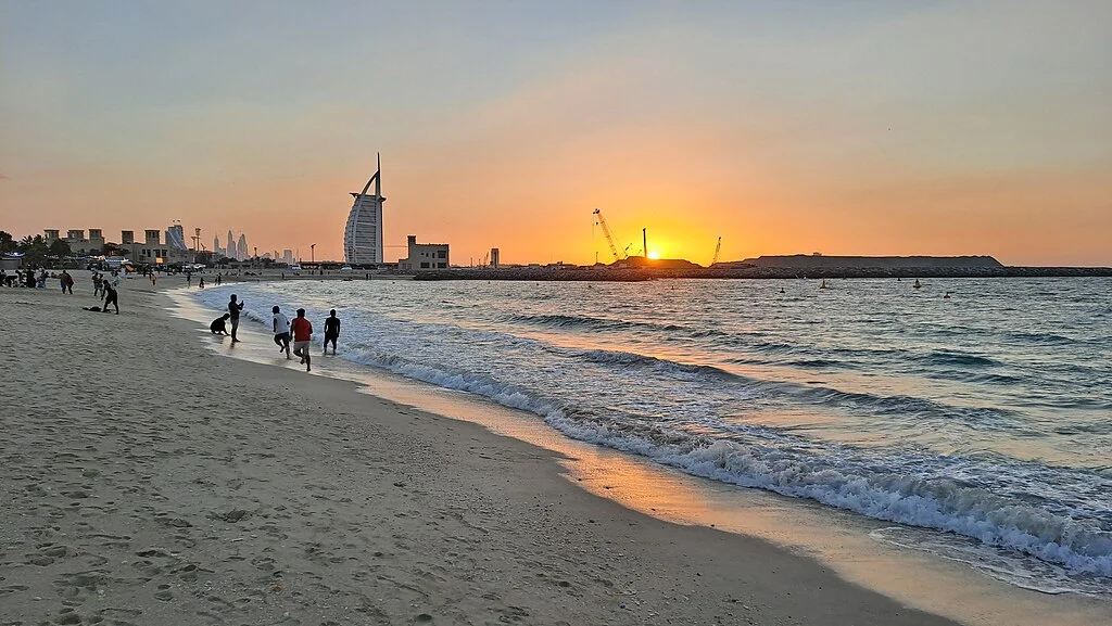 Breathtaking sunset at Al Sufouh Beach in Dubai with the iconic Burj Al Arab in the background. The golden hues reflect on the gentle waves, creating a serene coastal view.